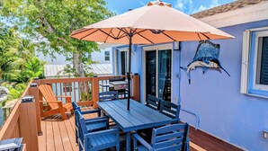 Een houten terras met een tafel, stoelen en een parasol, en een decoratieve vis aan de muur.
