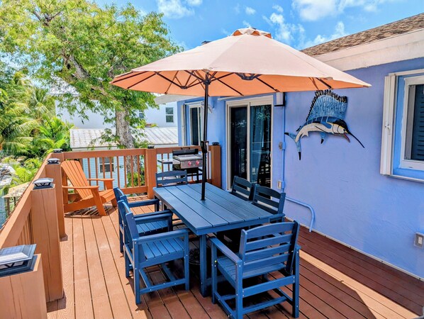 A wooden deck with a table and chairs, an umbrella, and a decorative fish on the wall.