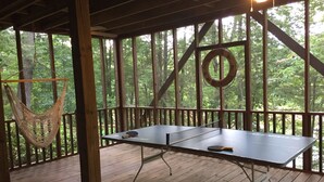 Une table de ping-pong sur une terrasse en bois, avec un hamac et un anneau suspendu.