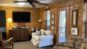 Un salon chaleureux avec un ventilateur de plafond, un téléviseur, des murs en bois, un canapé, un fauteuil à motifs et des certificats encadrés accrochés au mur.