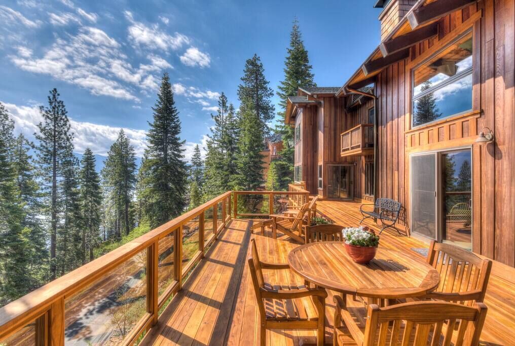 Eine Holzterrasse mit rundem Tisch und Stühlen, umgeben von hohen Bäumen.