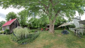 A rustic wooden cabin with a red roof, a picnic table, and a large tree in a backyard.