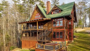 Une cabane en bois avec un toit vert, un balcon et une véranda couverte.