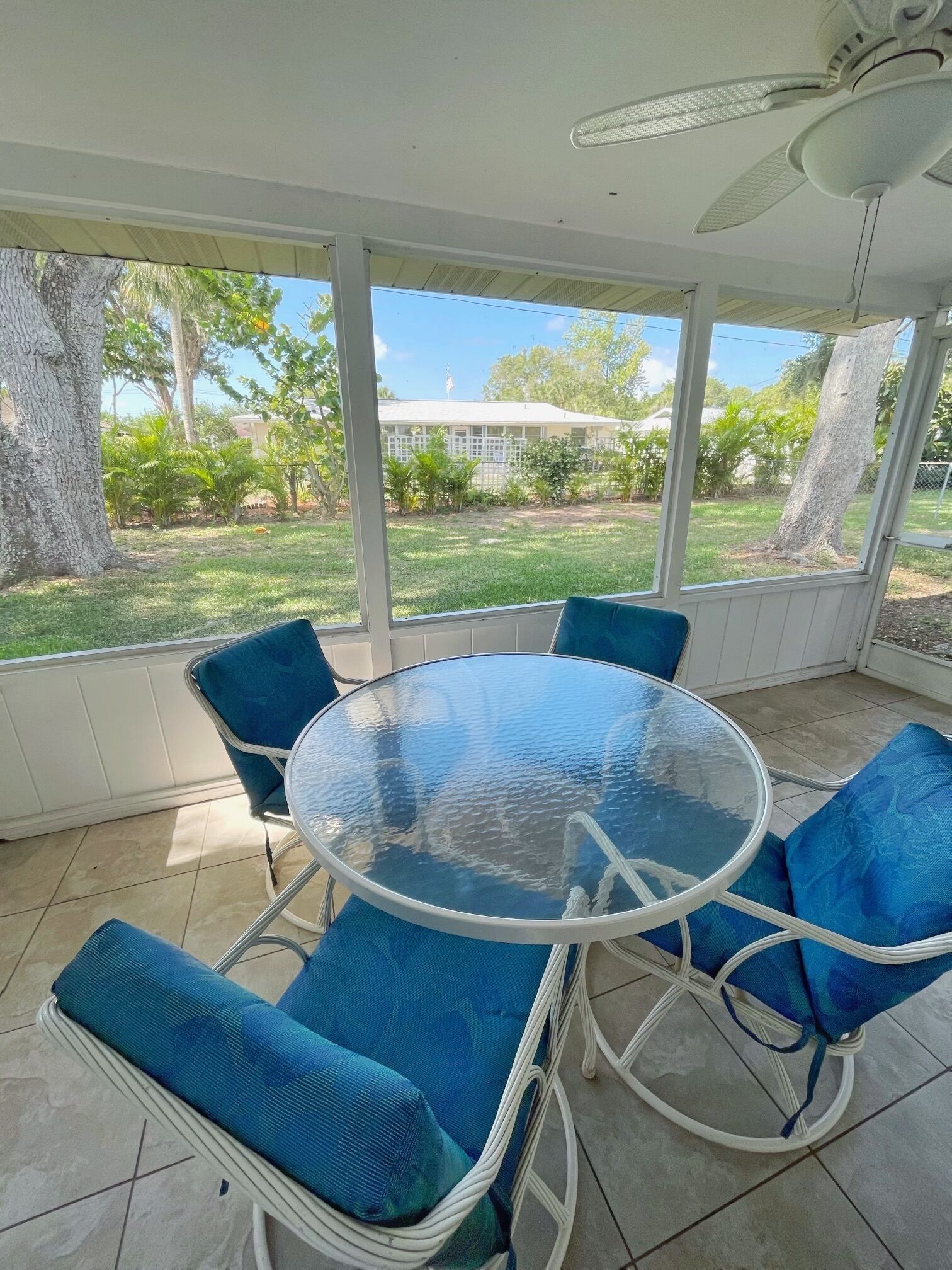 A covered patio with a round glass table and blue cushioned chairs.