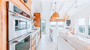 Une cuisine moderne dotée de fours encastrés, d’un îlot central et de luminaires suspendus.