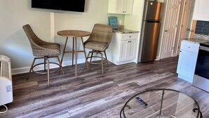 A kitchen with a flat-screen TV, two wicker chairs, a small round table, white cabinets, a stainless steel refrigerator, and a glass-top coffee table. - SunnyDaze-Brand new reno- King bed, Free bikes! (Hilton Head Island)