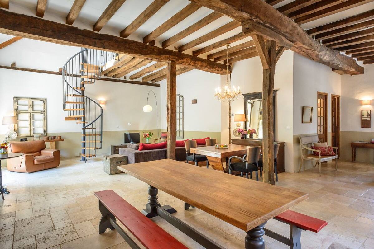 Un amplio salón con una mesa de comedor de madera, bancos y una escalera en espiral.