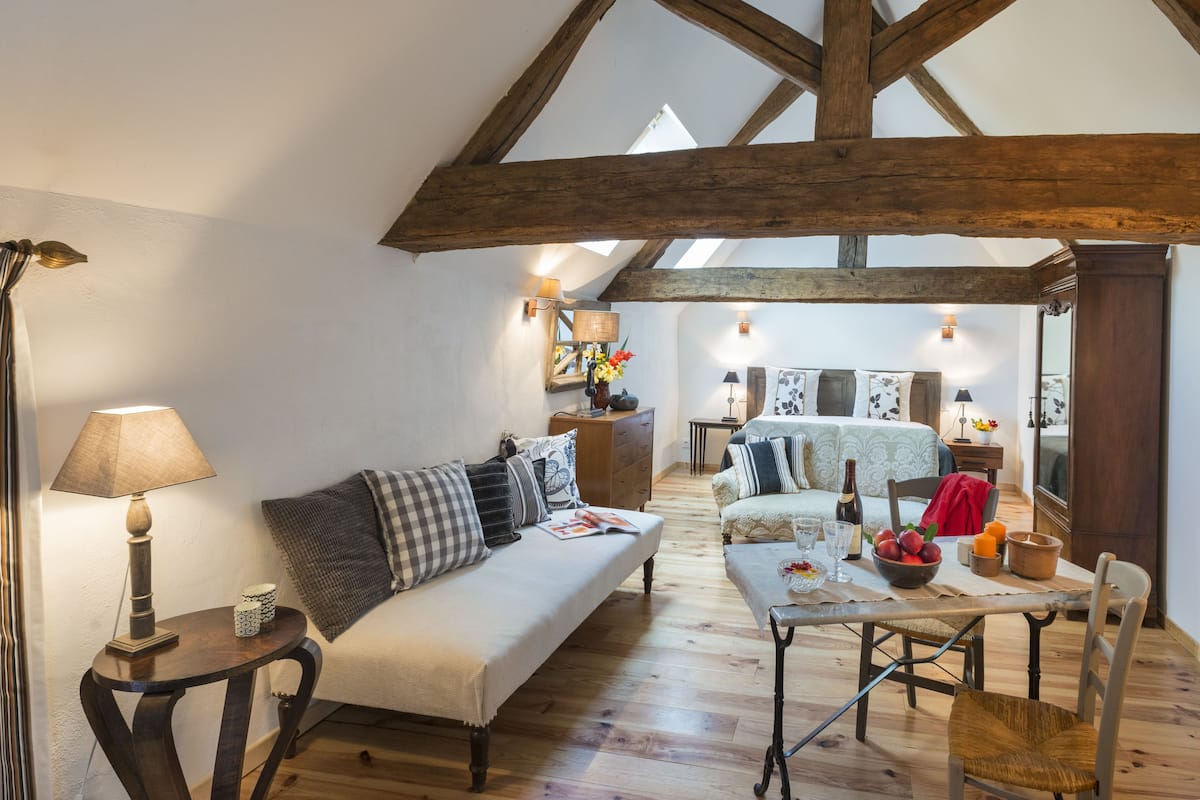 Una habitación acogedora con techo de madera, un sofá, una mesa de comedor con sillas y una pequeña mesita de noche con lámpara.