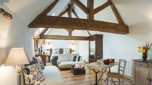 Ein gemütliches Zimmer mit Holzbalkendecke, einer Couch, einem Tisch mit einer Vase und einer Lampe.
