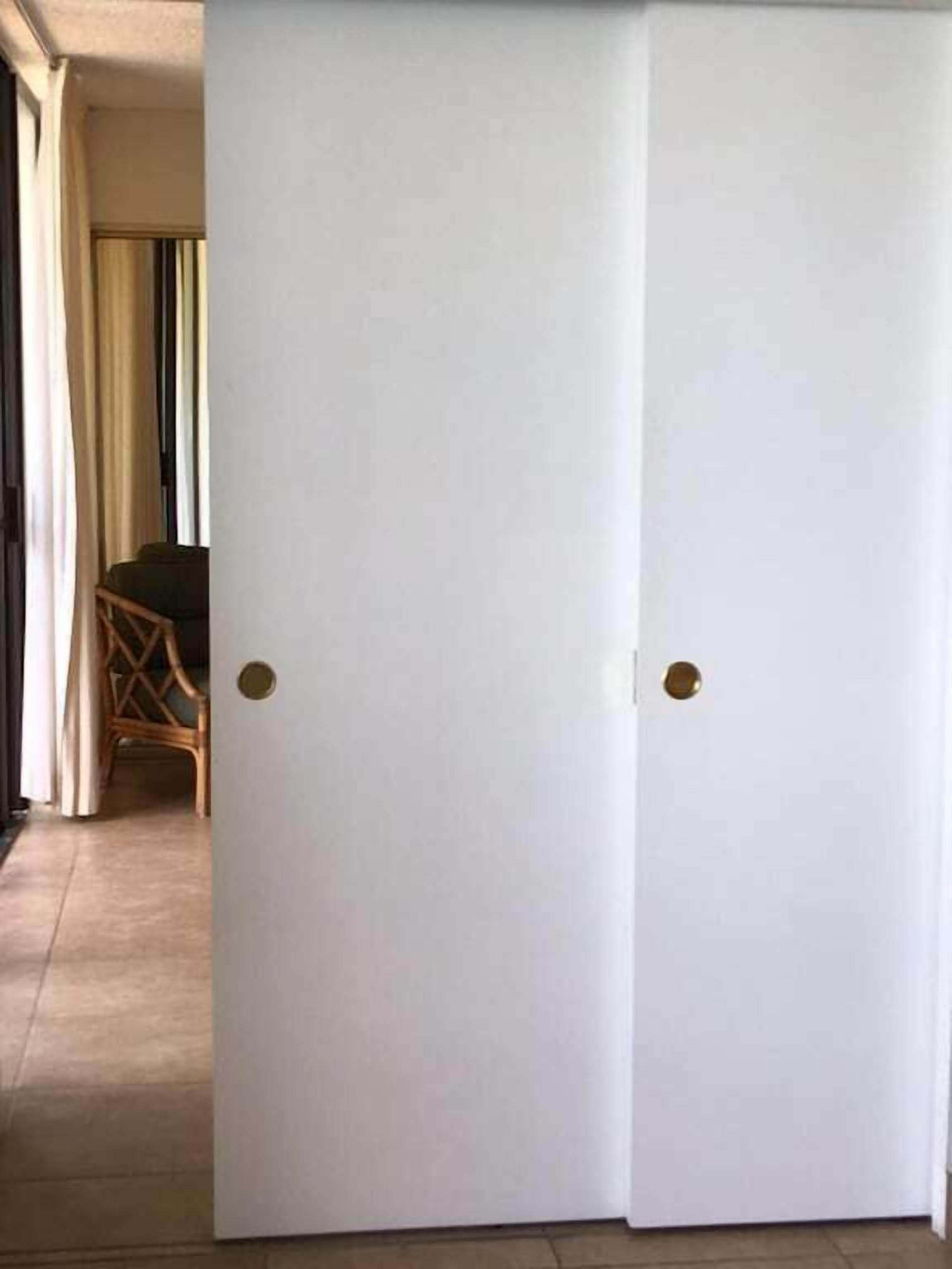 Uma porta branca fechada com puxador de latão, que dá para um quarto com chão de azulejos e uma cadeira de vime visível pela abertura.