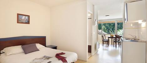 A modern hotel room with a large bed, a small desk, and a view of the garden through the window.