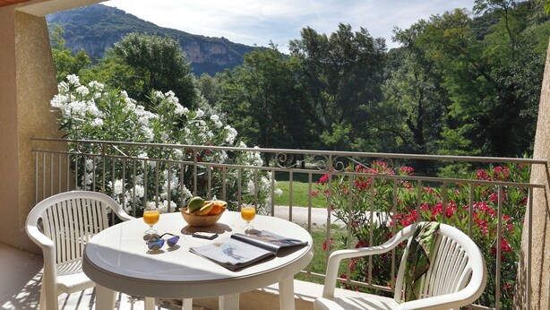 A balcony with a table set for two, featuring a basket of fruit, a glass of orange juice, and a magazine. - Vacancéole - Le Domaine de Chames (Vallon-Pont-d'Arc)