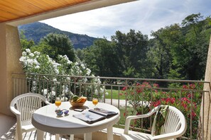 A balcony with a table set for two, featuring a basket of fruit, a glass of orange juice, and a magazine. - Vacancéole - Le Domaine de Chames (Vallon-Pont-d'Arc)
