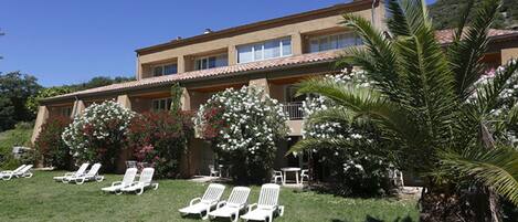 Un edificio su due piani con tetto in tegole, un balcone e un prato curato con poltrone da relax bianche.
