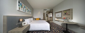 A hotel room with a large bed, a bedside table with a lamp, a wall-mounted TV, and a framed sign above the bed.