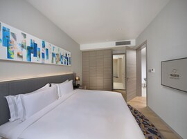 Una habitación de hotel moderna con una cama grande, una mesita de noche, una obra de arte abstracta en la pared y un cartel enmarcados con el logo de Frasers Hospitality.