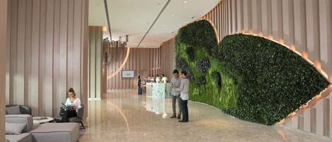 A modern lobby with a reception desk, seating area, and a green wall feature.