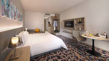 A modern hotel room with a bed, bedside table, lamp, desk with chair, and a TV mounted on the wall.