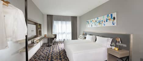 Una habitación de hotel con una cama grande, un escritorio, una silla, un armario y una ventana con cortinas.