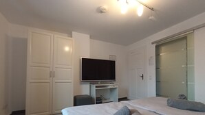 A hotel room with a bed, a TV, a wardrobe, and a bathroom with a glass door. - Fettehenne Gästehaus (Erkrath)