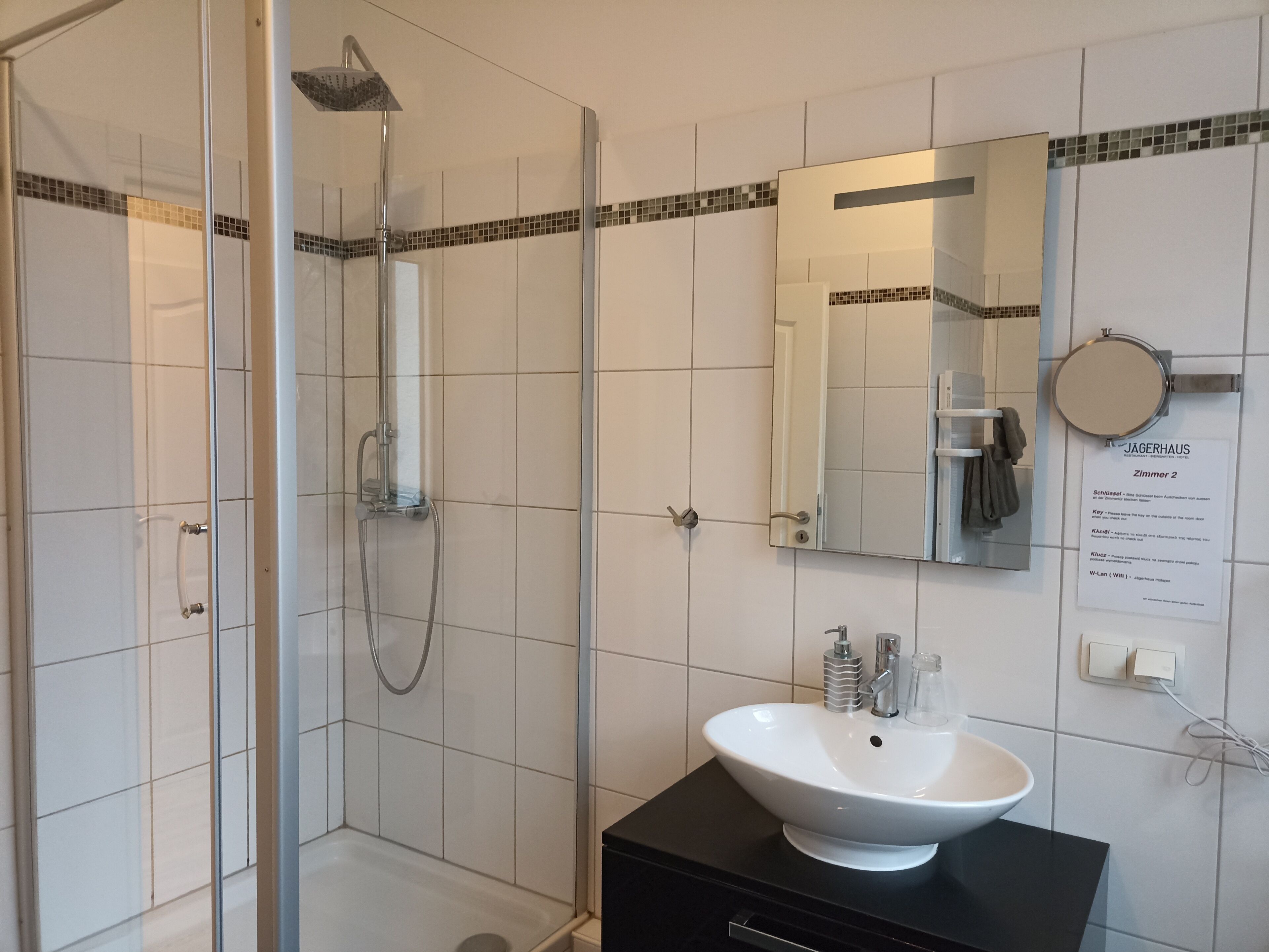 A modern bathroom with a glass-enclosed shower, a white sink with a black countertop, and a mirror above the sink.