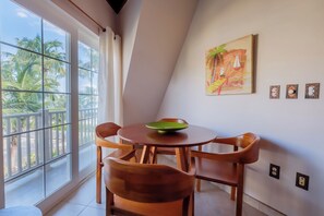 A dining area with a table and chairs, a painting on the wall, and a view of palm trees through large windows. - Newly Remodeled Three Bedroom Beachfront Condominium at The Landings (San Pedro)