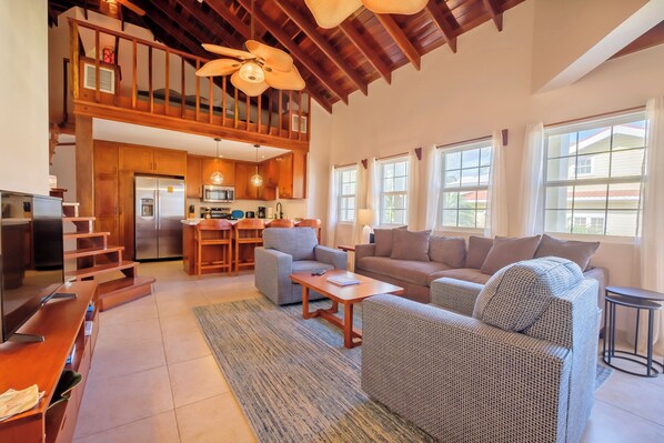 A spacious living area with a high ceiling, wooden beams, a kitchen in the background, and large windows. - Newly Remodeled Three Bedroom Beachfront Condominium at The Landings (San Pedro)