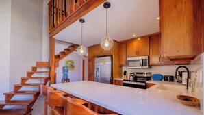Una cucina moderna con mobili in legno, un'isola centrale con posti a sedere, elettrodomestici in acciaio inossidabile e una scala che conduce a un piano superiore.