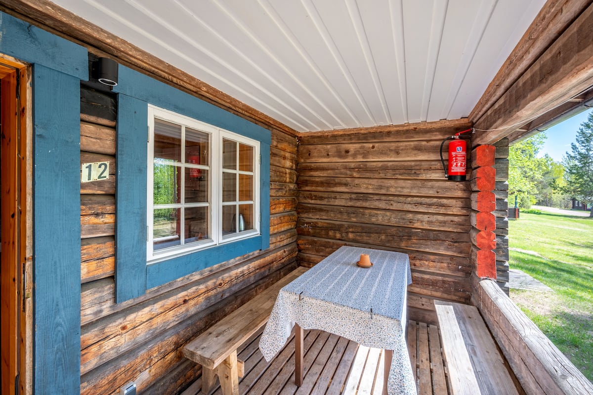 A log cabin with a number 12 sign, a window, a table with a tablecloth, and a fire extinguisher.