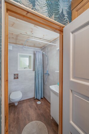 Une petite salle de bain comprenant des toilettes, un lavabo, une douche et une fenêtre.