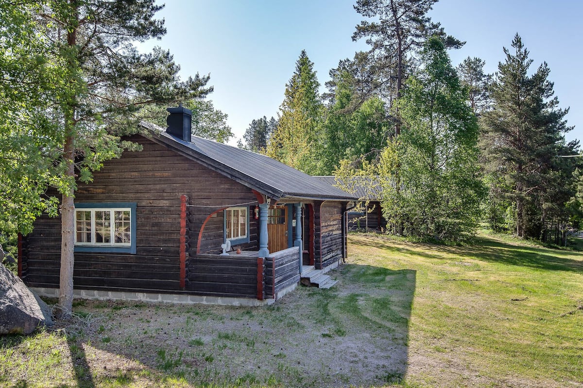 A log cabin with a porch, surrounded by trees.