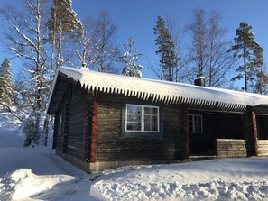 Une cabane en rondins dont le toit et les fenêtres sont recouverts de neige, entourée d’arbres et de neige.
