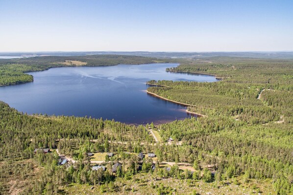 Une vue aérienne d’un lac entouré d’une forêt dense, avec plusieurs maisons et un ciel dégagé.