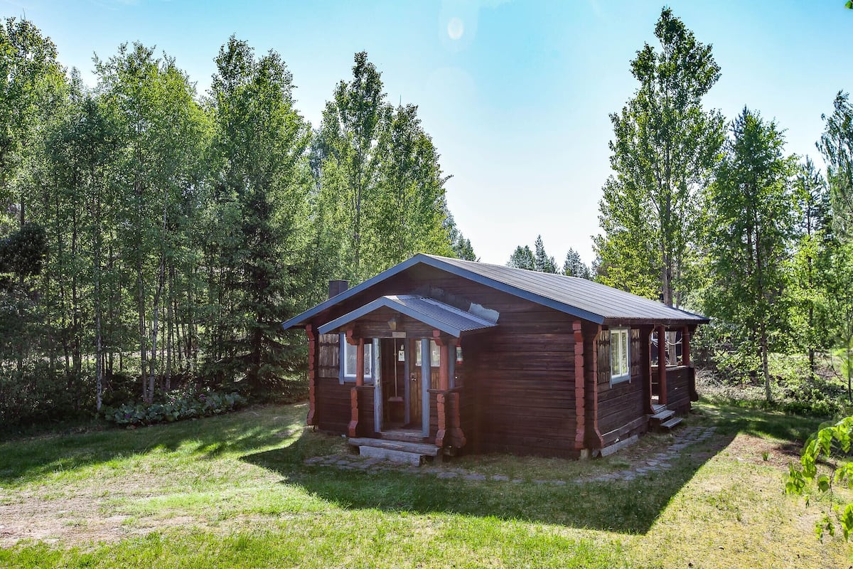 A small, rustic cabin with a gabled roof, surrounded by a forest.