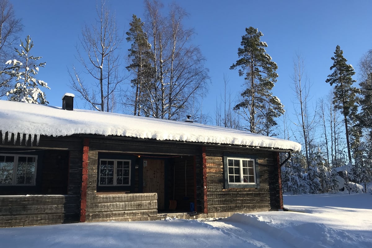 A log cabin with a snow-covered roof, wooden walls, and a front porch.
