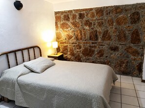 Un lit avec une tête de lit, une lampe de chevet et un mur en pierre.
