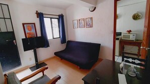 Una sala de estar con sofá, televisor, mesita y ventana con cortinas.