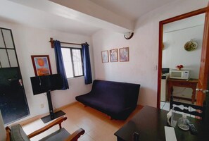 Una sala de estar con sofá, televisor, mesita y ventana con cortinas.