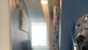 A laundry room with a washing machine, a radiator, a window, and a towel rack.