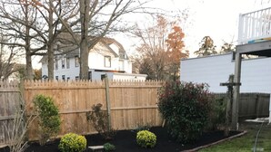 A backyard with a wooden fence, a small garden with various plants, and a grassy area.
