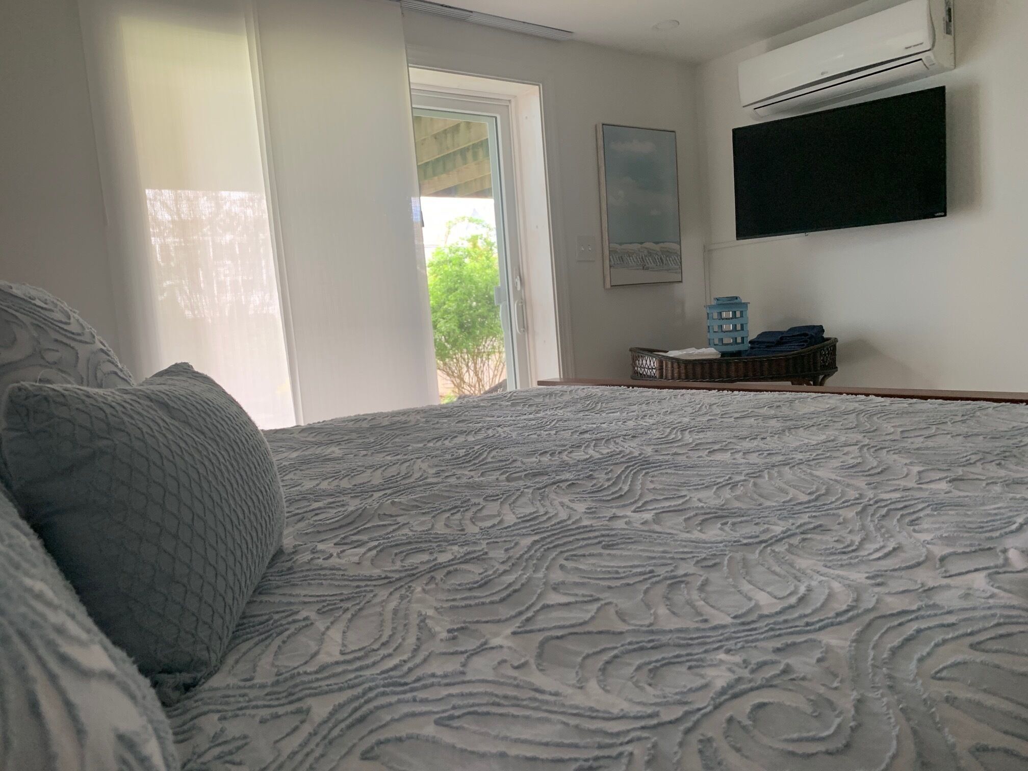Un dormitorio con una cama grande, una ventana con cortinas, un aire acondicionado montado en la pared y un cuadro enmarcado.