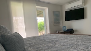 A bedroom with a large bed, a window with curtains, a wall-mounted air conditioner, and a framed picture.