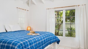 A bedroom with a bed, a window with curtains, a lamp, and a view of greenery outside. - Romantic Getway Steps from the Beach (Providenciales)
