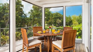 A wooden deck with a round table and four chairs, a glass of orange juice, a plate with a croissant, and a pitcher of orange juice. - Romantic Getway Steps from the Beach (Providenciales)