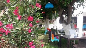 Un área de estar al aire libre con una mesa y sillas, rodeada de follaje y flores rosadas.
