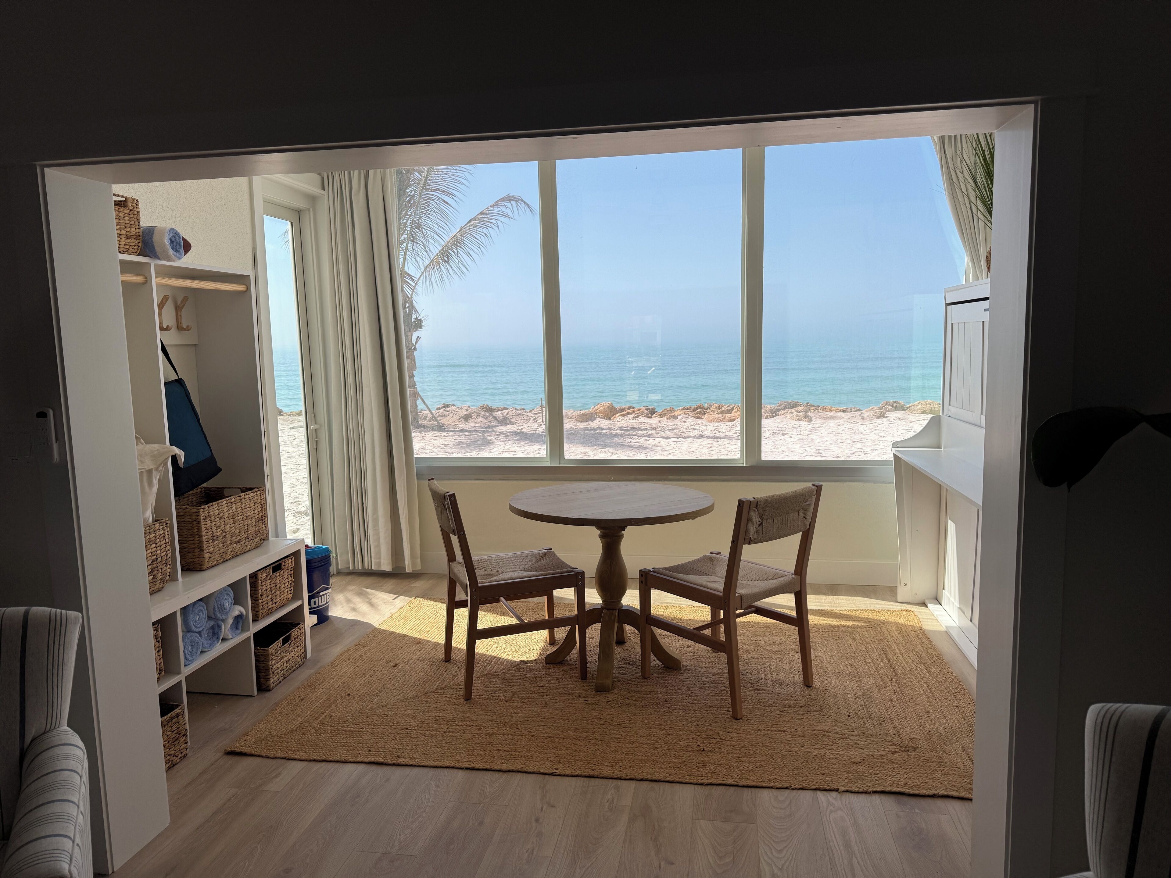 Una habitación con vistas a la playa, una mesa redonda con sillas y estantes con cestas.