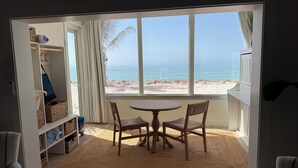 A room with a view of the beach, a round table with chairs, and shelves with baskets. - Beachfront Ground Level Suite - Everything is Modern & New (Siesta Key)