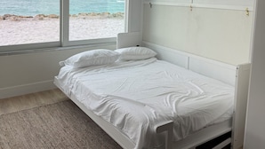 A bedroom with a bed, a ceiling fan, a large window with a view of the beach, and a small plant on a shelf. - Beachfront Ground Level Suite - Everything is Modern & New (Siesta Key)