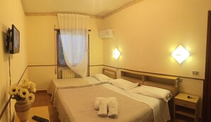 Habitació d'hotel amb dos llits, televisió, un ram de flors i finestra amb cortines.