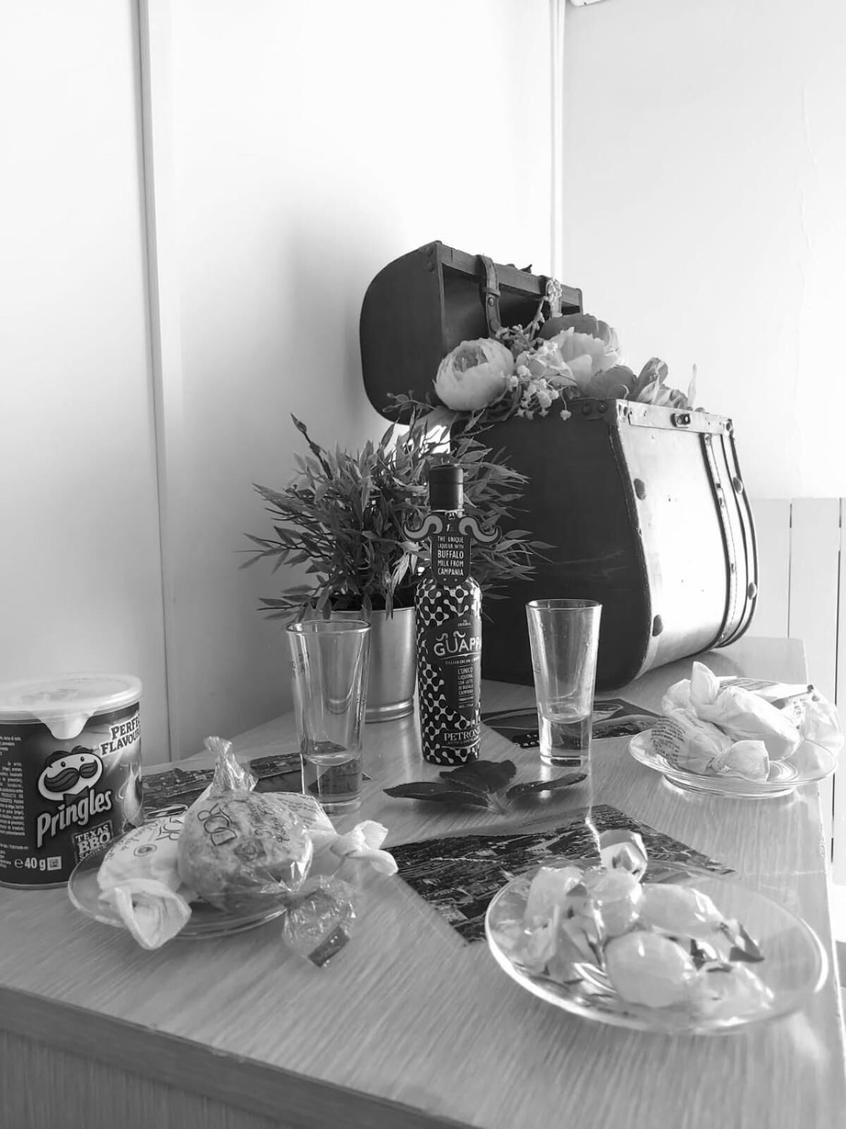 A table with a can of Pringles, a bottle of Guappo, a potted plant, and a guitar case.